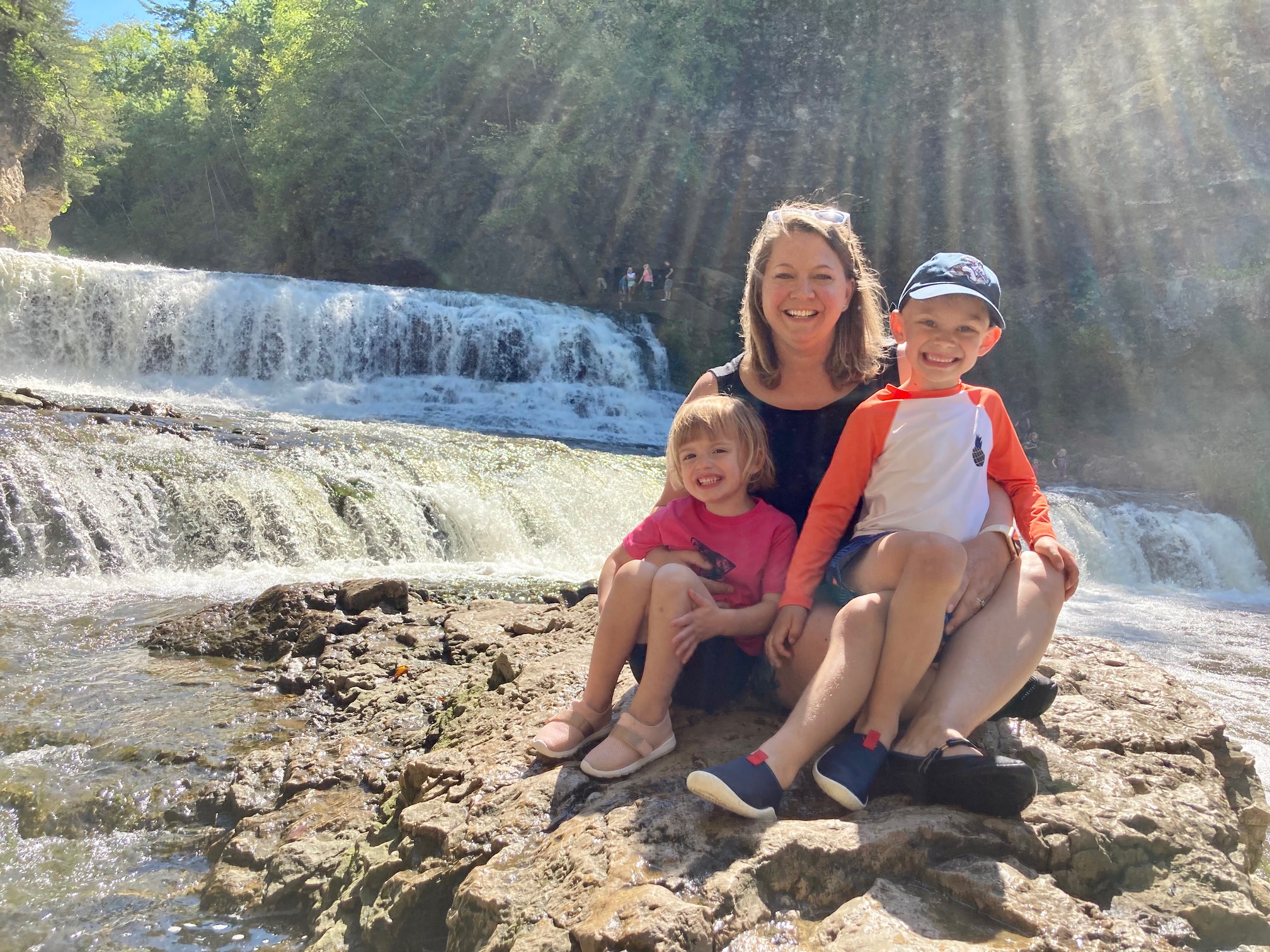a family photo of Amy Martin with her two kids, perched on a rock with a waterfall in the background