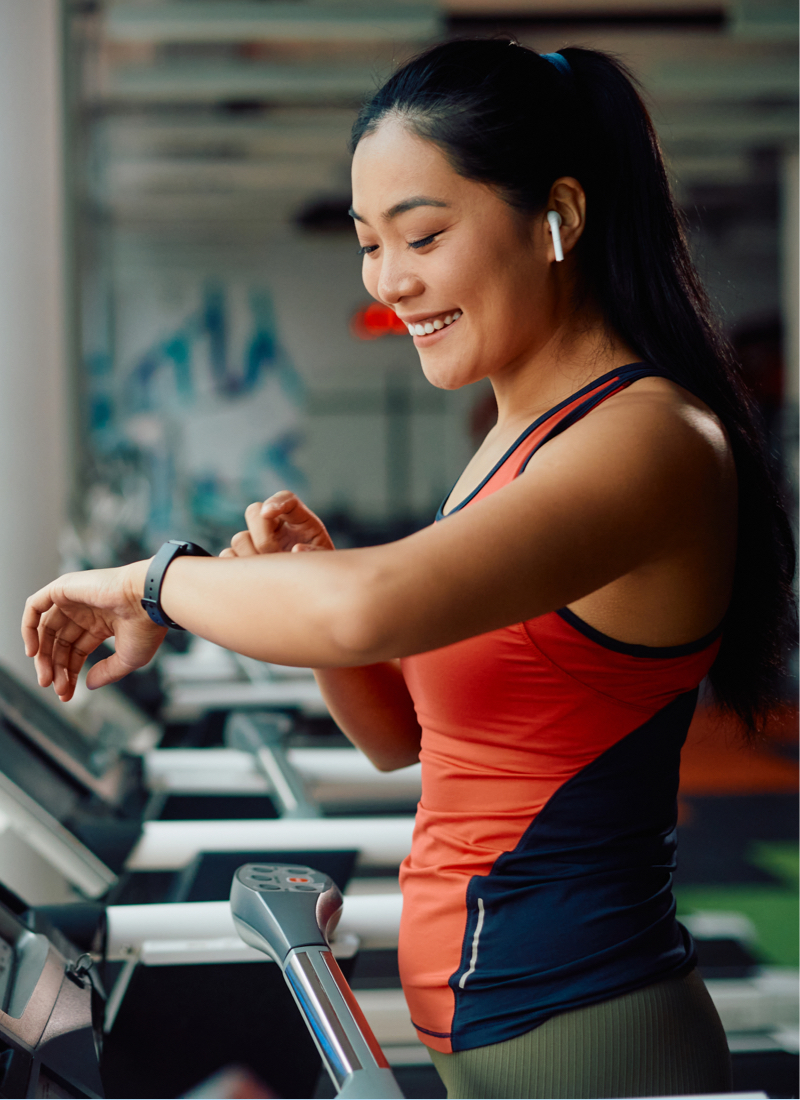 A woman smiles on a treadmill as she checks her smart watch. 