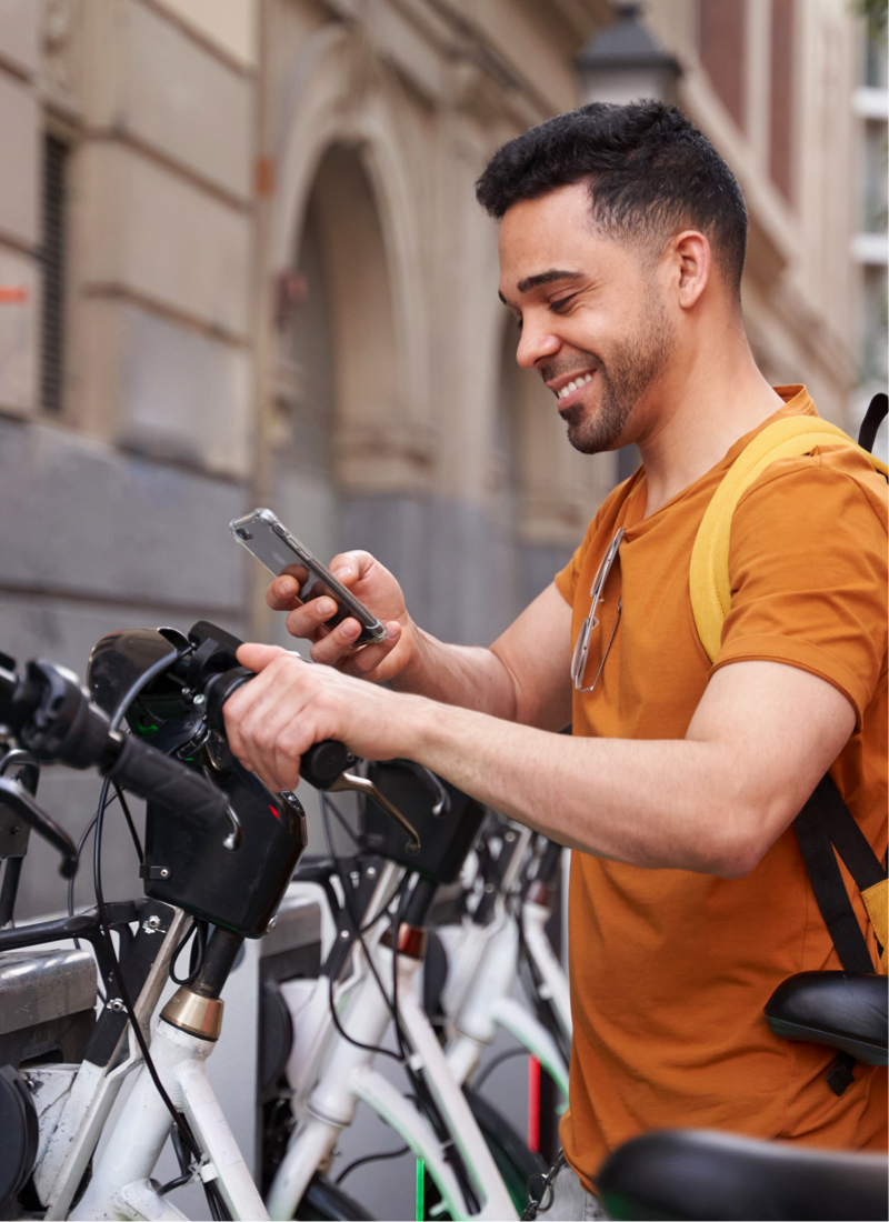 A man uses his cell phone to unlock a bike at a public bike docking station. 